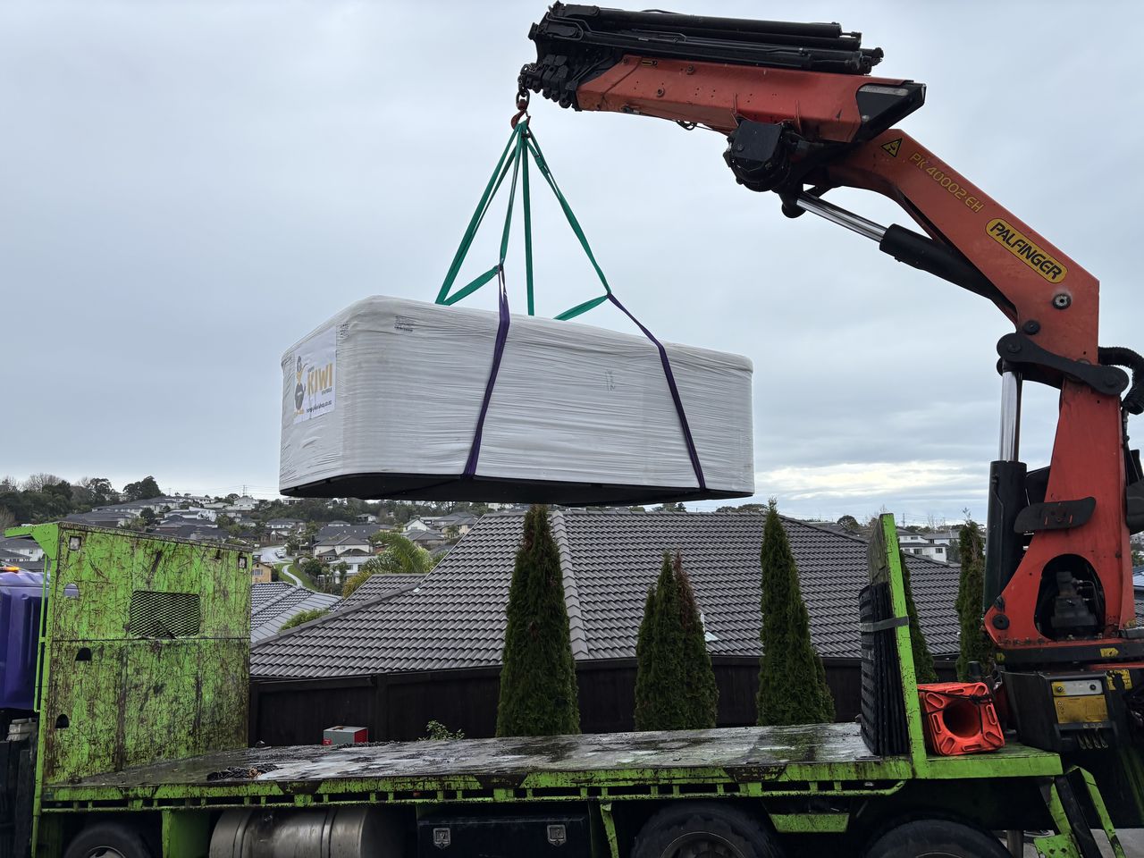 A large white unit lifted by crane over the roof of a house