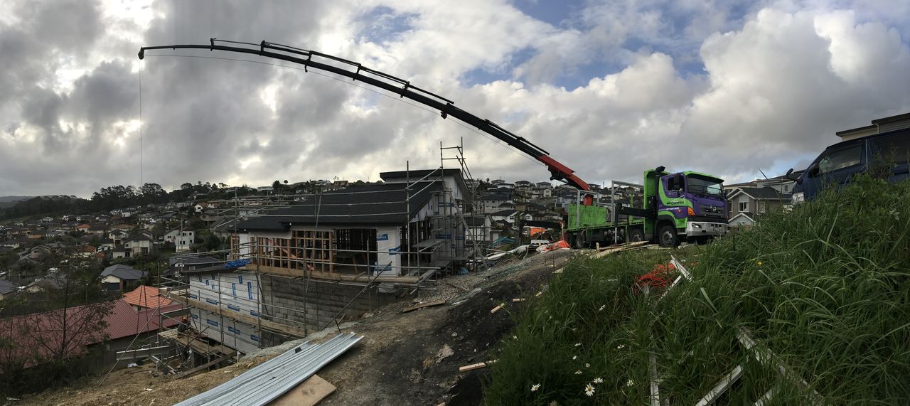 The crane boom extended over a house under construction on a hillside