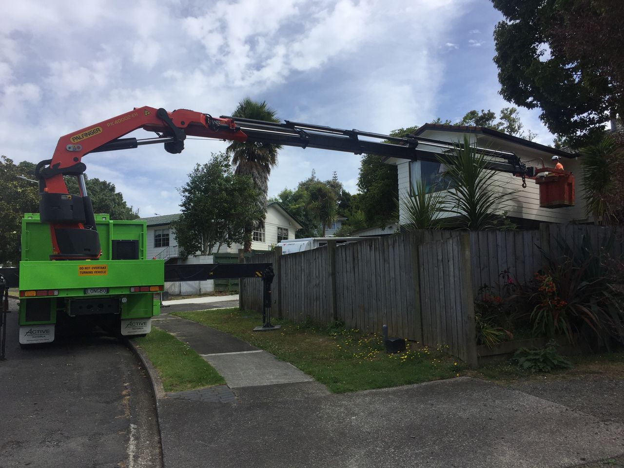 Crane boom extended over a house from a residential driveway