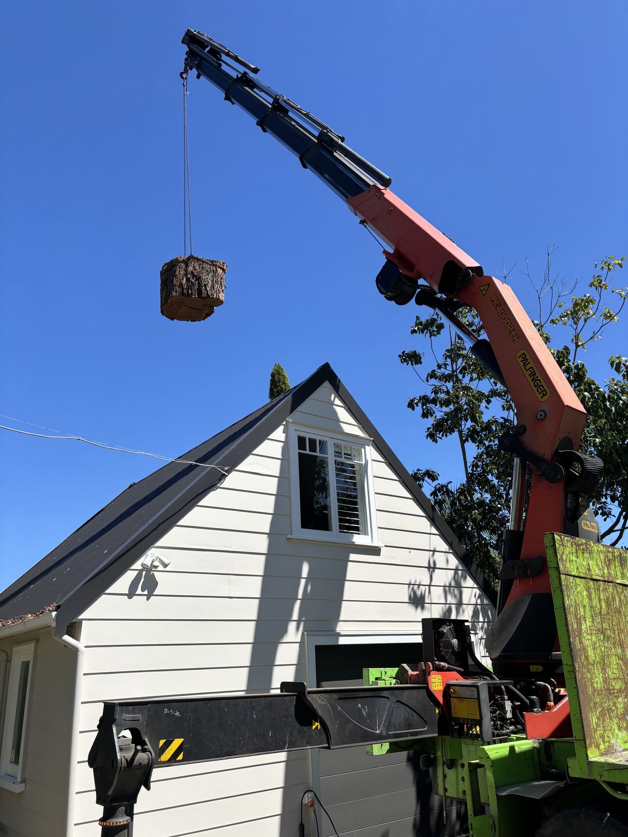 Crane lifting a tree section clear of a house roof